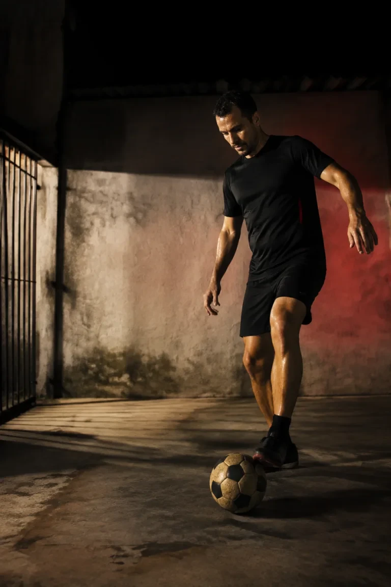Homem treinando com uma bola num beco à noite